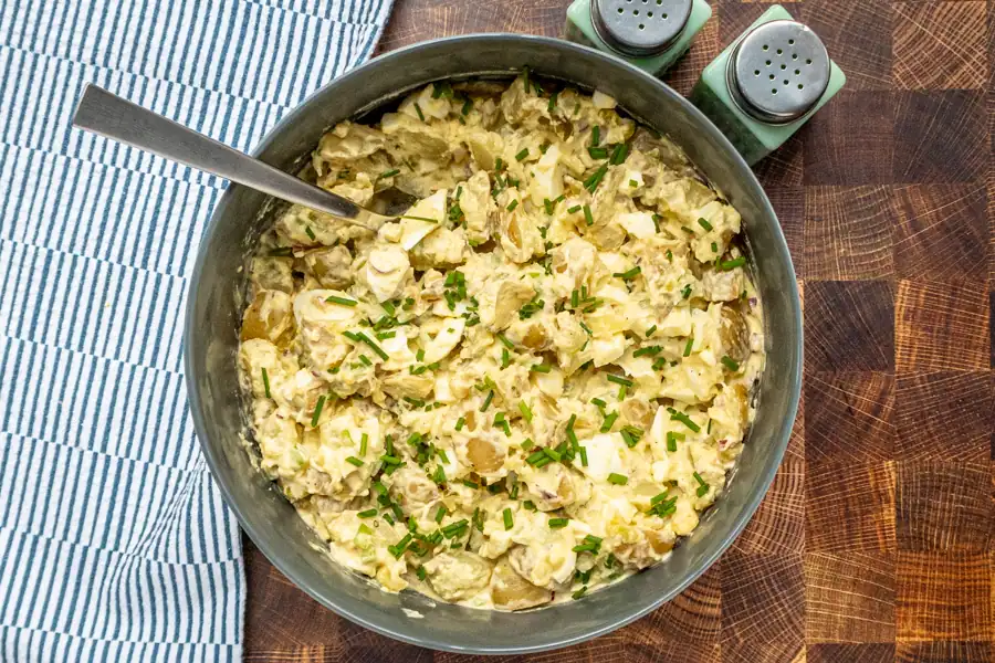 A serving bowl with the finished potato salad garnished with chives.