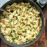 Creamy potato salad garnished with chopped chives on a dark wooden table.