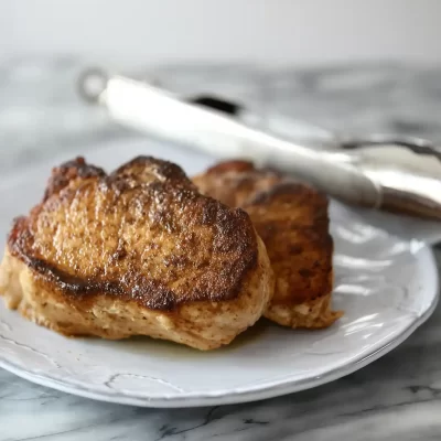 Grilled chicken thighs on a white plate with tongs nearby.