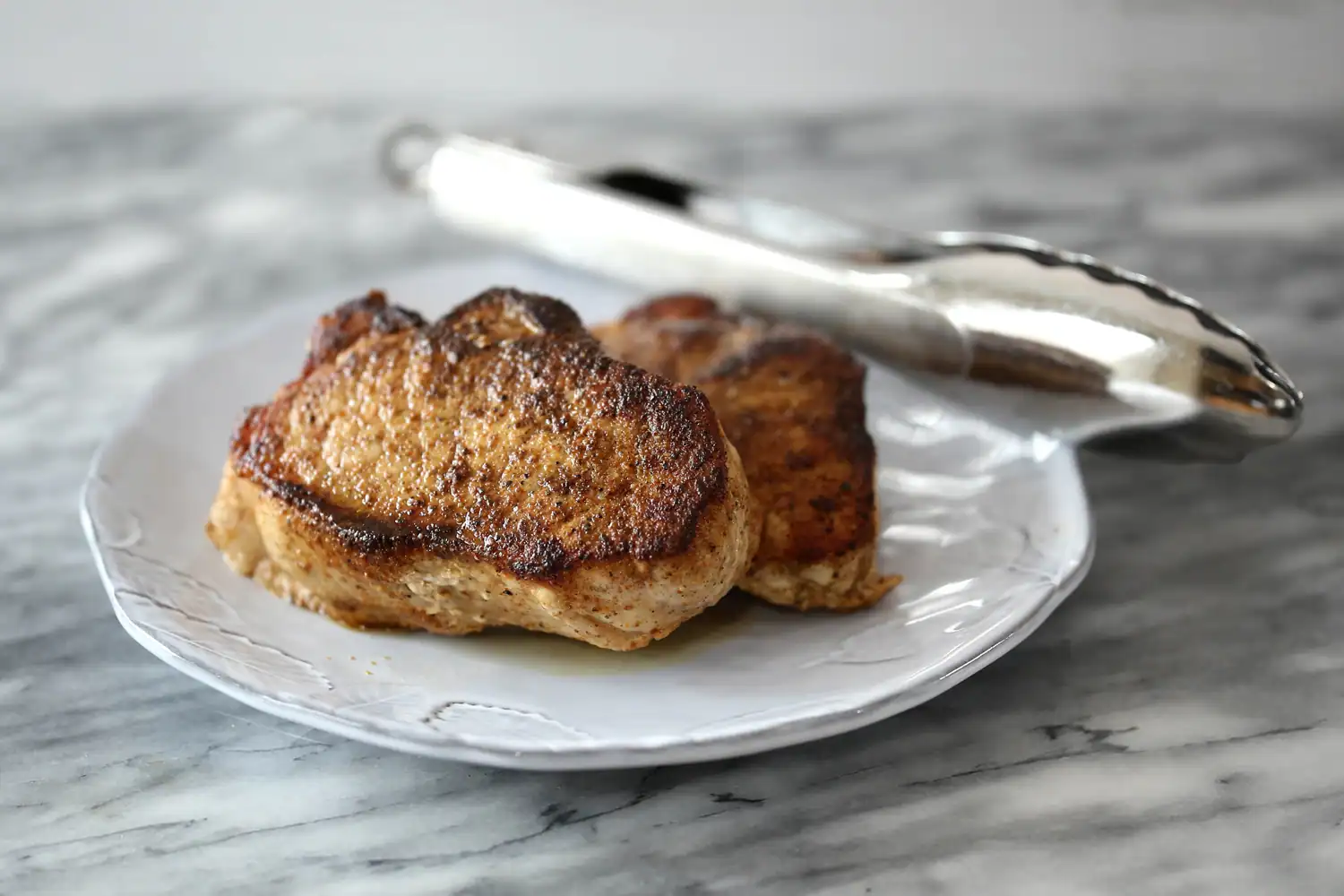 Instant Pot pressure cooker pork chops on a serving plate with tongs in the background.