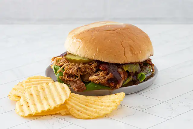 A pulled chicken sandwich topped with pickles and extra BBQ sauce.