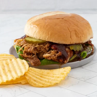 Slow-cooked pulled pork sandwich with barbecue sauce and pickles.