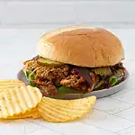 Tender shredded pork barbecue sandwich with pickles on a bun, served with crispy potato chips.