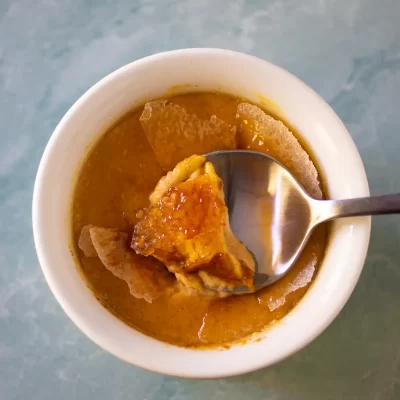 Creamy chicken soup with bread chips and melted cheese in a white bowl.