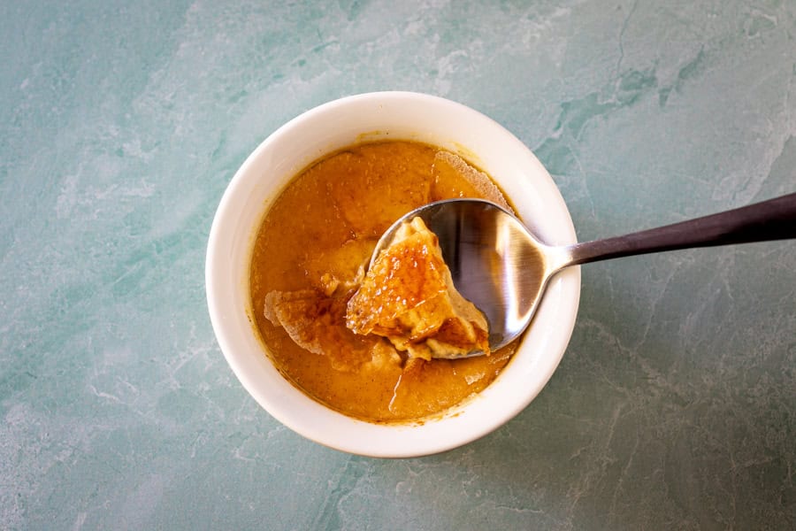 Pumpkin crème brûlée in a ramekin with a spoon showing the cracked top.