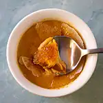 Smooth, brown stew with chunks of ingredients in a white bowl.