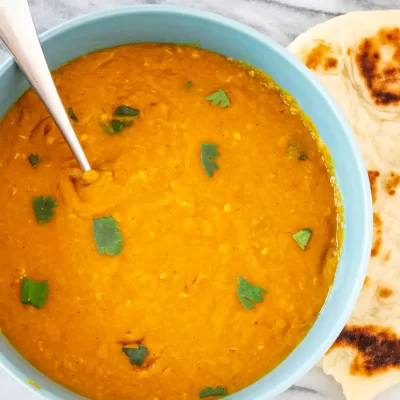 Creamy lentil soup garnished with fresh cilantro, served with toasted naan bread.