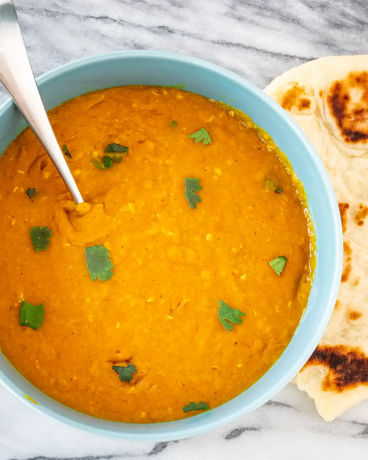 Creamy lentil soup garnished with fresh cilantro, served with toasted naan bread.