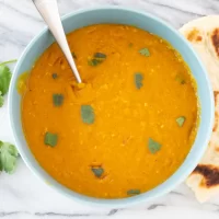 Butter chicken curry in a bowl garnished with cilantro and served with naan bread.