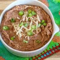 A bowl of Instant Pot pressure cooker refried beans garnished with shredded cheese and green onions.