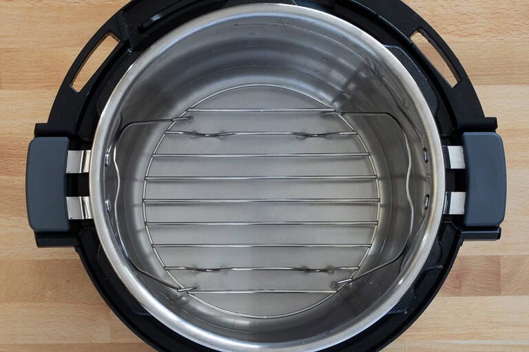 Stainless steel inner pot with a wire rack inside a pressure cooker.