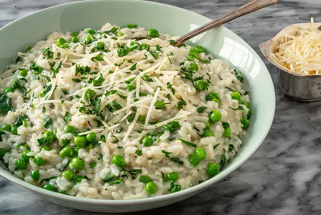 A bowl of Instant Pot risotto with spinach and peas, with a garnish of parsley and Parmesan cheese.
