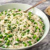 A bowl of Instant Pot risotto with spinach and peas, with a garnish of parsley and Parmesan cheese.
