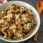 Cooked chicken and stuffing mixture topped with chopped herbs in a white bowl.