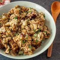 Cooked chicken and stuffing mixture topped with chopped herbs in a white bowl.