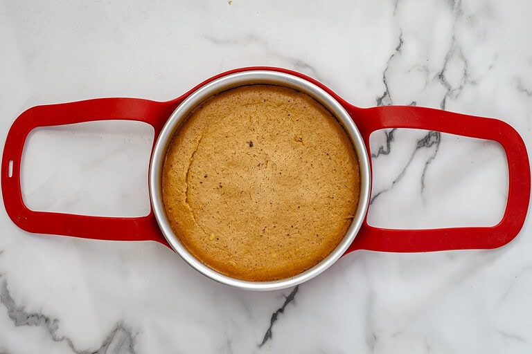 Golden baked cheesecake in a round metal pan with red handles.