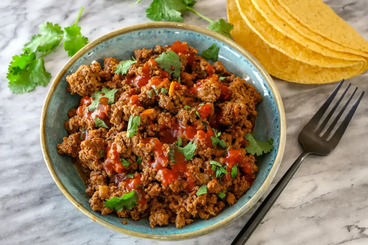A bowl with Instant Pot taco meat, with taco shells and cilantro on the side.
