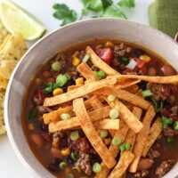 A bowl of Instant Pot taco soup with cheese, cilantro, and tortilla chips for garnish.