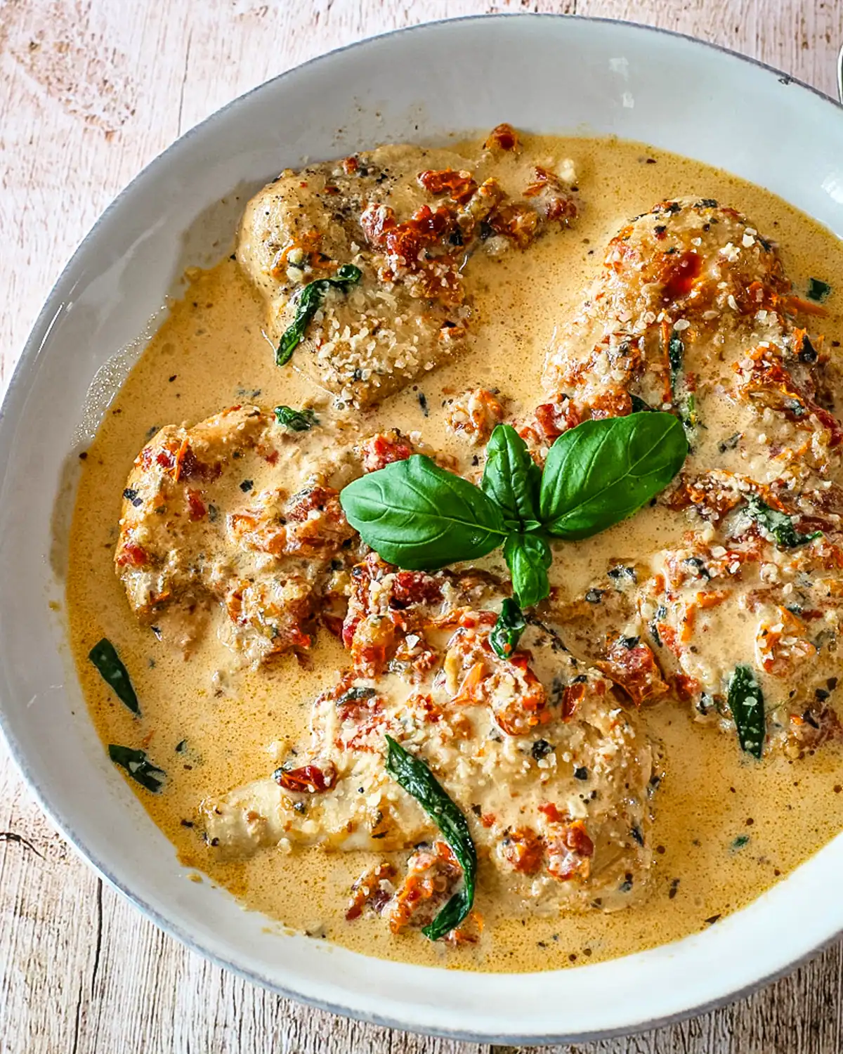 Creamy chicken in a flavorful sauce with basil garnish on a white dish.