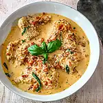 Creamy chicken curry garnished with fresh basil leaves and sliced chili peppers.