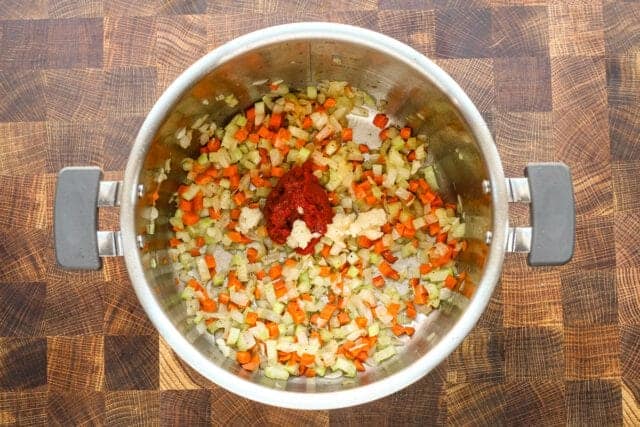 Diced onions, carrots, and spices in a stainless steel pot.