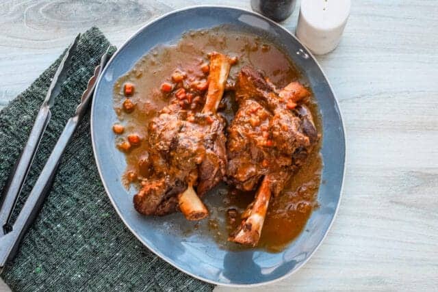 Succulent braised beef shanks in rich sauce on a blue plate.