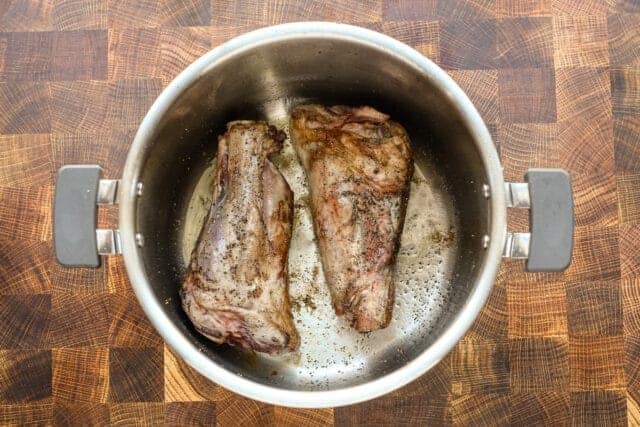 Searing two beef short ribs in a stainless steel pot.