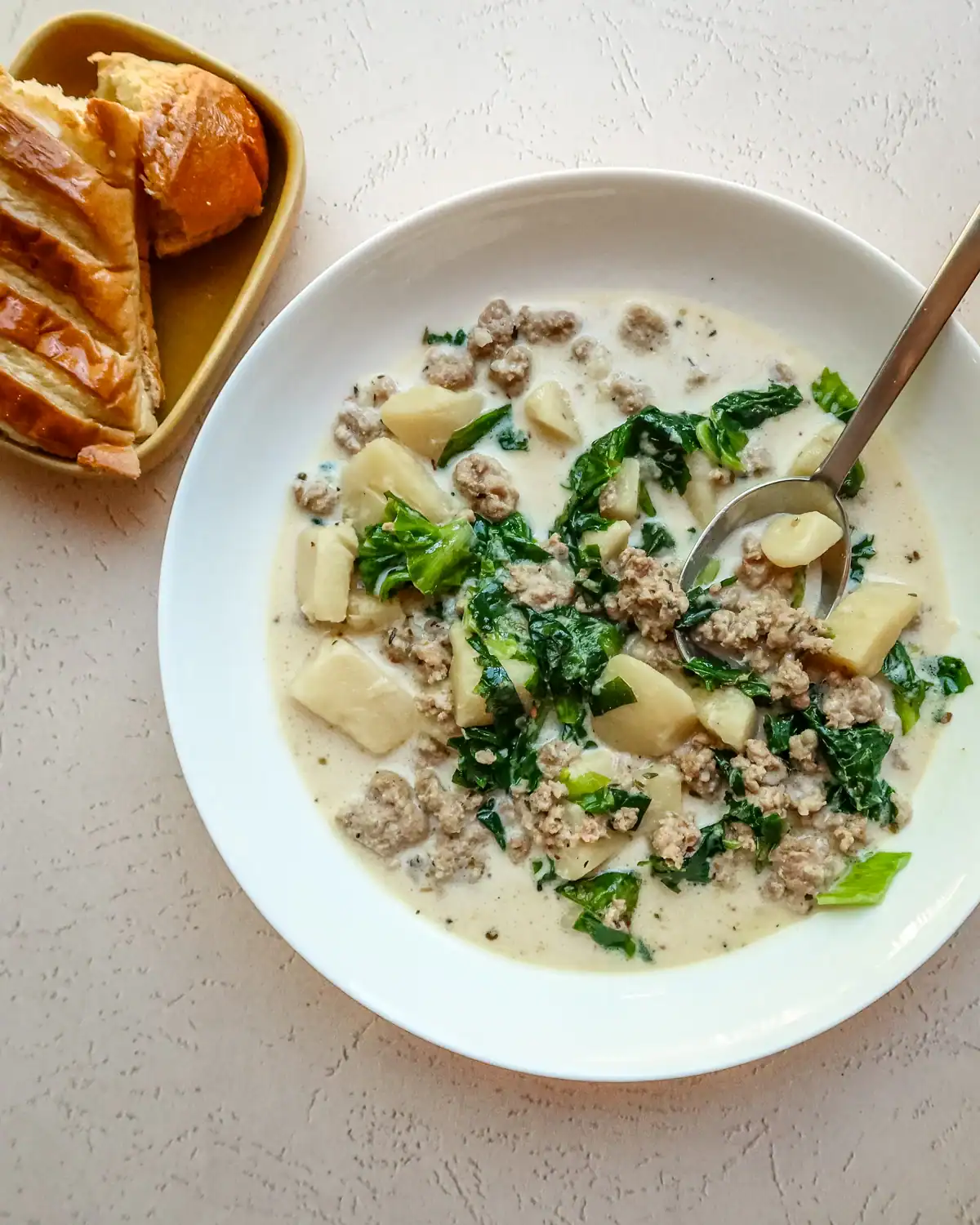 Savory ground meat potato and kale soup in a white bowl on a textured surface.