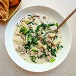 Creamy sausage and potato soup with greens in a white bowl.