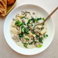 Creamy sausage and potato soup with greens in a white bowl.
