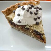 A slice of chocolate chip pie on a plate with whipped ceam and mini chocolate chips.