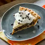 Dessert slice with whipped cream and chocolate chips on dark plate.
