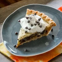 Dessert slice with whipped cream and chocolate chips on dark plate.
