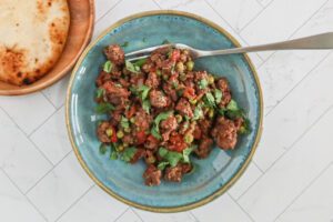 A serving of keema matar in a turquoise bowl with fork, and naan bread on the side.