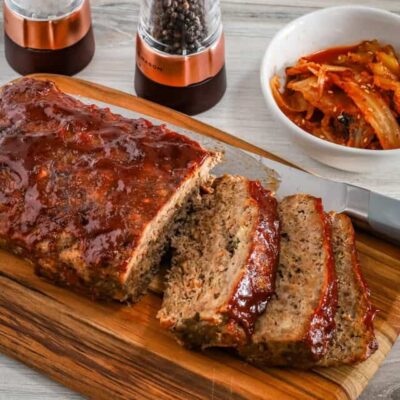 Korean meatloaf on a cutting board, sliced with kimchi on the side.