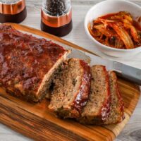 Korean meatloaf on a cutting board, sliced with kimchi on the side.