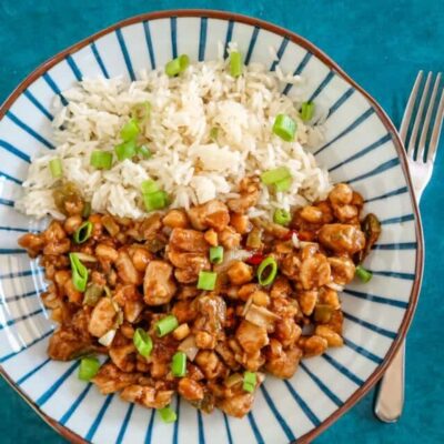 Steamed white rice and sweet and sour chicken with green onions on a striped plate.