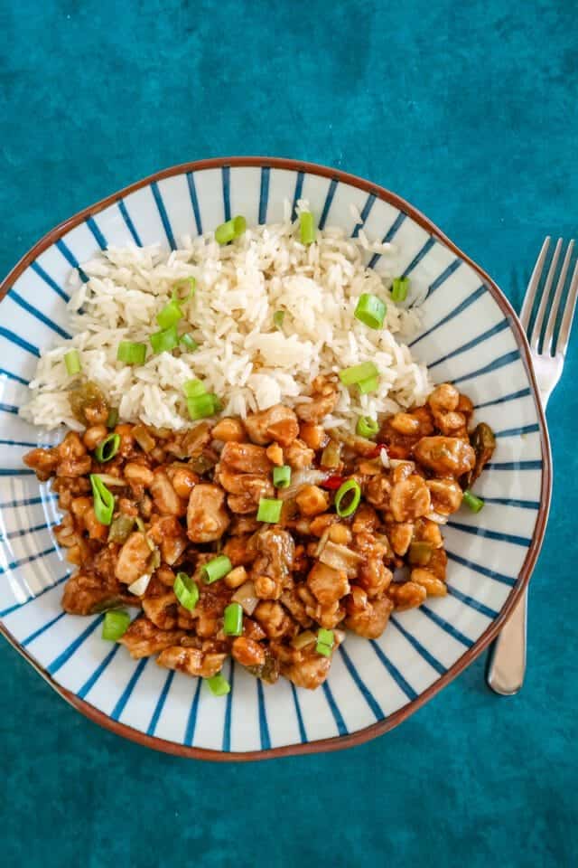 Steamed white rice and sweet and sour chicken with green onions on a striped plate.