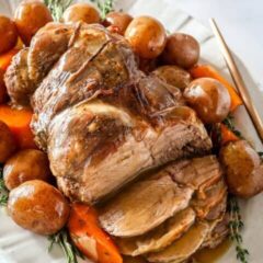 roast leg of lamb with gravy on a platter with vegetables