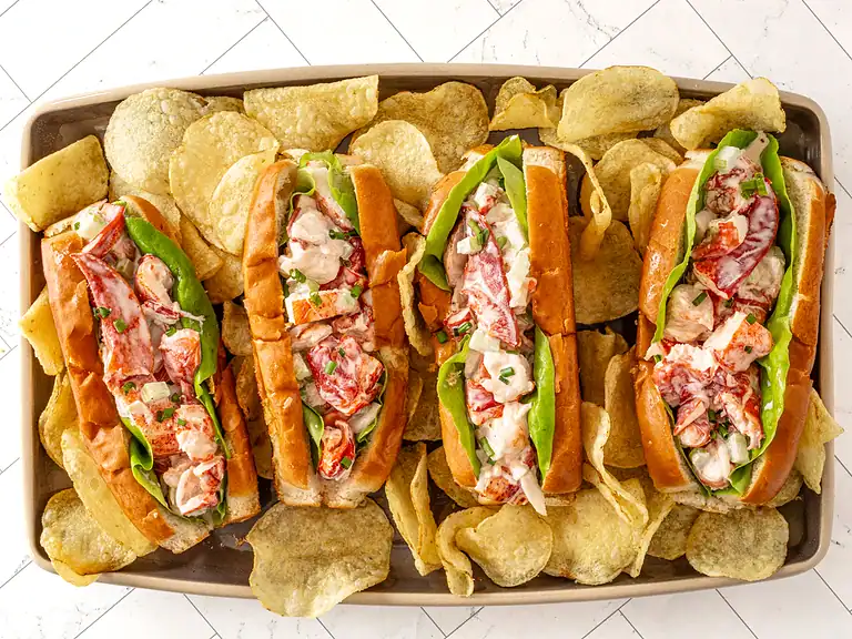 Lobster rolls with fresh lobster meat, lettuce, and tartar sauce in toasted buns, served with potato chips.