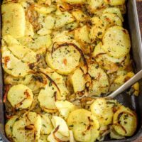 Golden roasted potato slices with herbs in a baking dish.