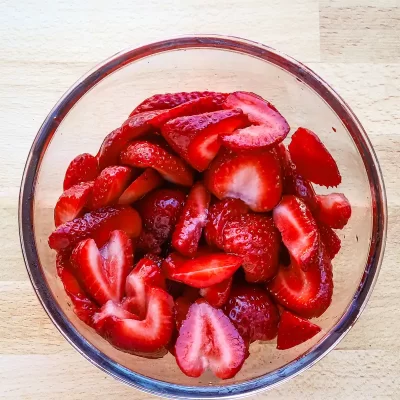 Fresh sliced strawberries in a glass bowl on a wooden surface.