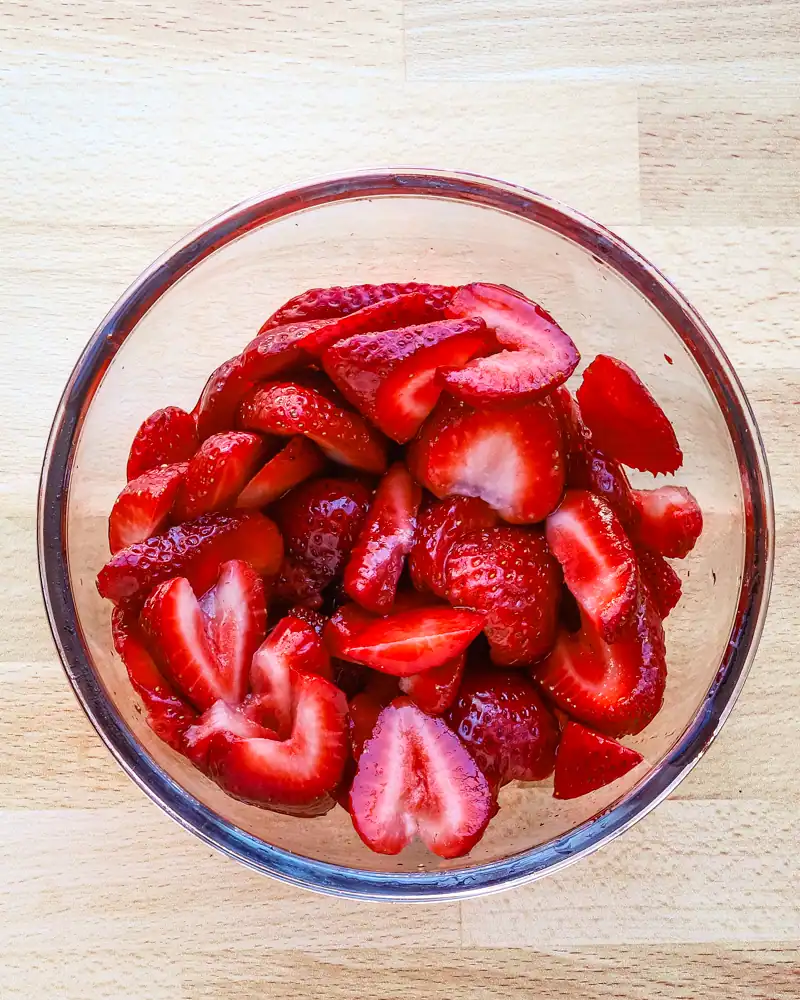 Fresh sliced strawberries in a glass bowl on a wooden surface.
