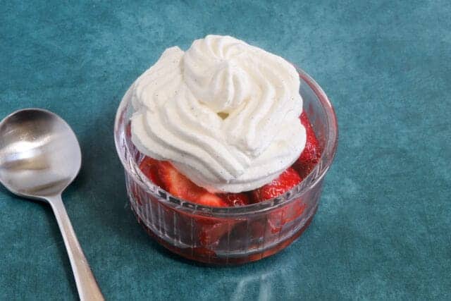 Sweet strawberry dessert topped with whipped cream in a glass bowl.