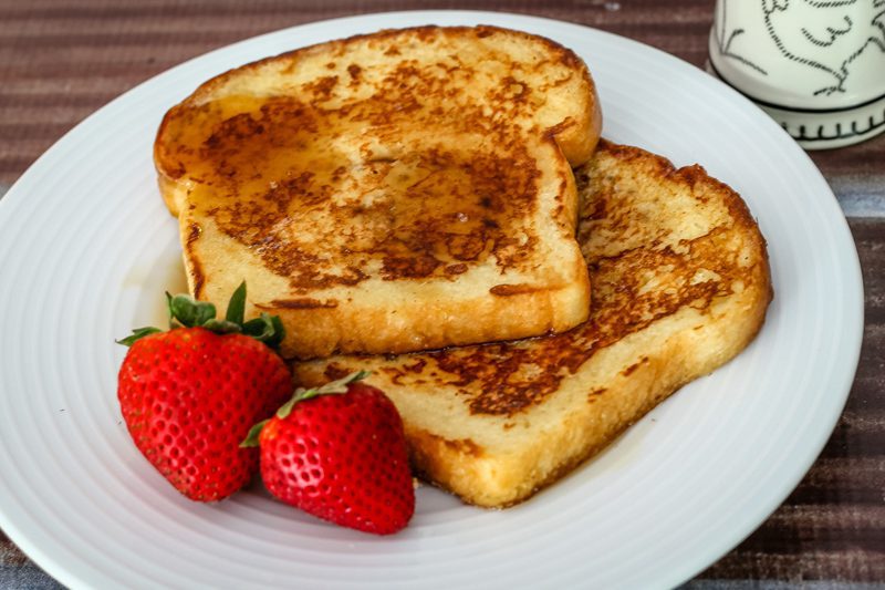 maple cinnamon french toast on a plate with a drizzle of maple syrup and fresh strawberries.