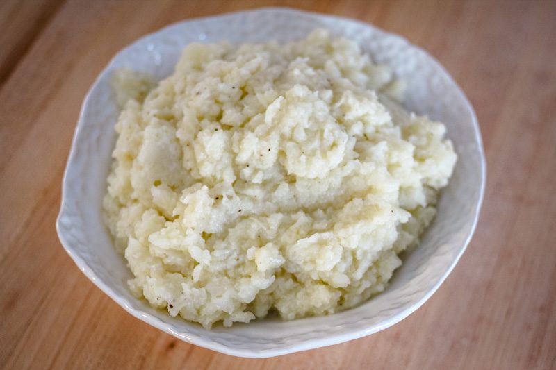 A bowl of fluffy mashed cauliflower made with butter, cream, garlic, and seasonings.