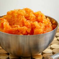 Mashed carrots and rutabagas in a bowl with nutmeg and nutmeg grater in the foreground.