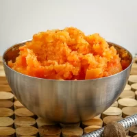 Creamy mashed sweet potatoes in a stainless steel bowl on wooden surface.