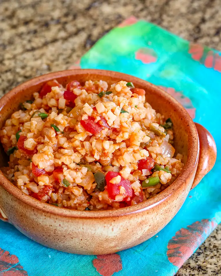 Bowl of cooked cauliflower rice with diced tomatoes and green onions.