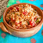 Cooked rice dish with chopped vegetables and tomato chunks in a brown bowl.